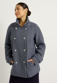 Veste à motif pied-de-poule bleu et noir avec un col haut, des boutons croisés et des poches latérales. Design en tissu texturé.