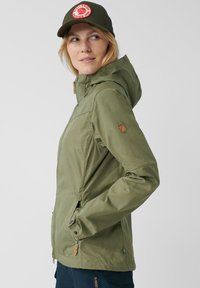 Olivgrön vattentät jacka med huva, med dragkedja fram, sidfickor och en läderlogotyp på ärmen. Lättviktsmaterial.