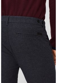 Donkergrijze gepatternde broek met een textuurafwerking, voorzien van een standaard tailleband, zijzakken en een zwart label op de achterkant.