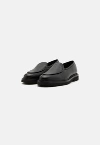 Black leather slip-on shoes with a smooth texture, rounded toe, and a low, flat sole. Features a subtle stitch accent along the edge.