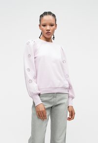 Lichtroze sweatshirt met pofmouwen en uitgesneden bloemenpatronen. Geribbelde manchetten en zoom versterken het textuurontwerp. Gecombineerd met grijze broek.