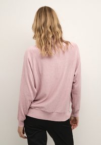 Világos rózsaszín, oversize pulóver hosszú ujakkal, bordás aljjal és mandzsettával, puha tapintással és laza szabással, hátulról nézve.