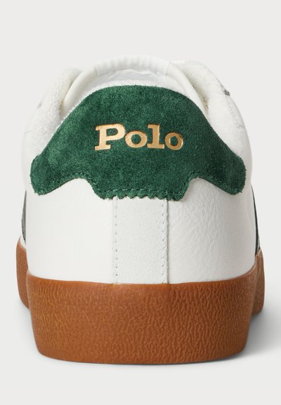 Vit lädersneaker med grön mocka-hälaccent, guld "Polo"-logotyp och strukturerad brun gummisula. Klassisk låg toppdesign.