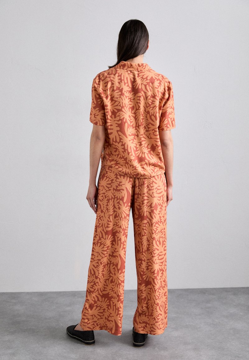 Short-sleeve, button-up shirt and wide-leg pants in orange with a coral abstract leaf pattern, made from lightweight fabric.
