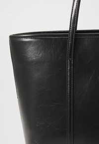 Zwarte leren tote bag met een gladde textuur, gestructureerde vorm en slanke, langgerekte hengsels met subtiele stiksels.