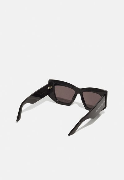 Occhiali da sole cat-eye neri con lenti scure e finitura lucida. Presentano angoli netti e logo inciso sulla tempia.