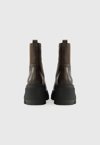 Καφέ δερμάτινες μποτίνες μέχρι τον αστράγαλο με ελαστικές πλευρές και χοντρές μαύρες καουτσούκ σόλες. Διαθέτουν λείο φινίρισμα και θηλιά για εύκολη φόρμα.