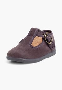 Zapato de ante morado oscuro con puntera redondeada, correa elástica y hebilla lateral. Presenta una suela de goma y un detalle de costura minimalista.