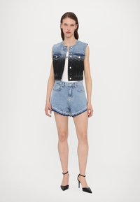 Must musta ja sinine denimist lühike vest, mis on varustatud nööbiga, koos helesiniste kõrge vöökohaga kulunud lühikeste pükste ja mustade kontsakingadega.