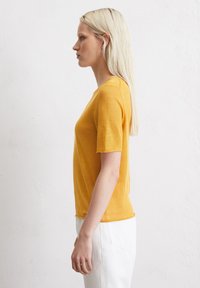 Geel T-shirt met korte mouwen en een ronde hals, gemaakt van een gestructureerde stof, gecombineerd met witte hoge taille broeken, zijaanzicht weergegeven.