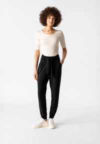 Svarta tapered byxor med knytmidja, i kombination med en ljus beige figurnära topp och vita sneakers. Slät textur och minimalistisk design.