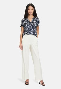 Blusa blu navy con motivo astratto bianco, maniche corte e scollatura a V, abbinata a pantaloni bianchi a vita alta e tacchi neri con cinturini.