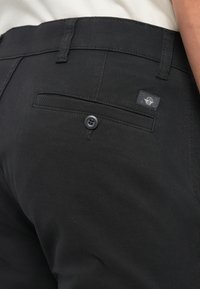 Pantaloni neri in tessuto testurizzato con una tasca posteriore con chiusura a bottone e un piccolo etichetta intrecciata sul retro.