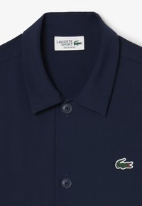 Polo shirt navy in tessuto testurizzato che presenta un colletto classico, due bottoni e un piccolo logo di coccodrillo verde sul lato sinistro del petto.