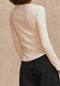 Top color beige chiaro a coste con maniche lunghe, caratterizzato da una cucitura centrale sul retro, abbinato a jeans neri a vita alta con un motivo sottile.
