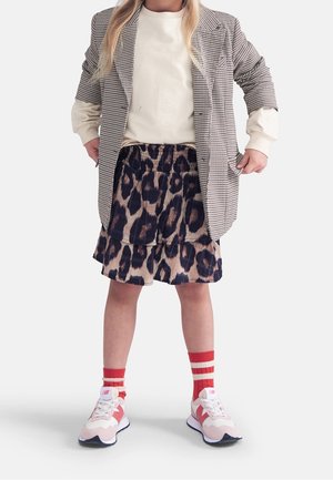 Enfant portant un blazer à pied-de-poule, un sweat crème, une jupe à motifs léopard et des chaussettes rayées rouges avec des baskets roses. Tenue décontractée en couches.