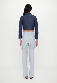 Modra denim jakna do pasu z dolgimi rokavi, v kombinaciji z svetlo modrimi hlačami visoko pasu, ki imajo na hrbtu prečnemo tkanino.