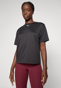 T-shirt de sport noir à manches courtes, en tissu léger et lisse, présentant un petit logo blanc sur le haut de la poitrine.