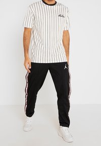 Vit randig t-shirt med svarta accenter, i kombination med svarta träningsbyxor med sidobranding och ett Jumpman-logotyp, bärs med vita sneakers.