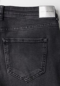 Jeans de mezclilla negra con una etiqueta plateada que dice "STREET ONE STUDIO." Incluye un bolsillo trasero y costuras de contraste a lo largo de las costuras.