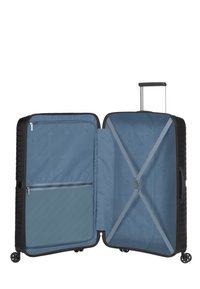 Valigia rigida nera con interno blu. Caratterizzata da una tasca con zip, cinghie incrociate per fissare gli oggetti e ruote scorrevoli.