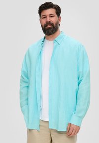 Turquoise button-up shirt van lichtgewicht stof, gelaagd over een witte ronde hals t-shirt. Casual pasvorm met lange mouwen en een ontspannen kraag.
