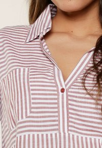 Camicia a righe con bottoni di colore rosa chiaro e bianco. Presenta un colletto, una tasca sul petto e un bottone rosso. Realizzata in tessuto leggero.