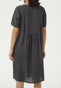 Harmaa pellavamekko lyhyillä hihoilla, gathered-taakse, sivutaskut ja polvenpituinen helma. Pehmeä rakenne ja omaa virtaavan siluetin.