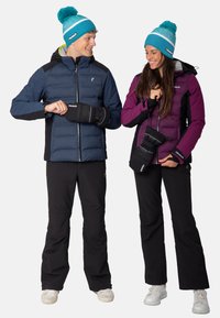 Two individuals wear outerwear: a navy blue puffer jacket and a purple insulated jacket. Both have black ski pants and matching mittens.