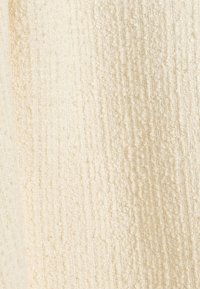 Geprepareerde stof in lichtbeige met een zachte, oneven oppervlakte. Bevat afwisselende ribbel- en lussenpatronen, wat de tactiele details benadrukt.
