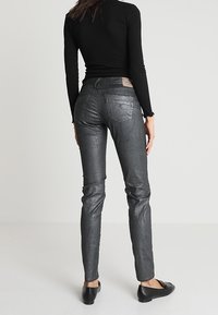 Pantalons taille haute ajustés en tissu métallique gris foncé avec une texture lisse, poches arrière et détails de surpiqûres.