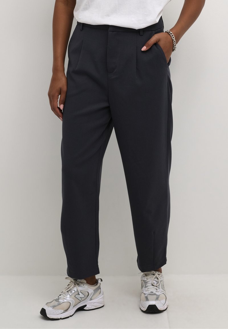 Pantalon bleu marine sur mesure avec une coupe décontractée, doté de deux plis avant et de poches latérales, associé à des baskets en maille argentée.