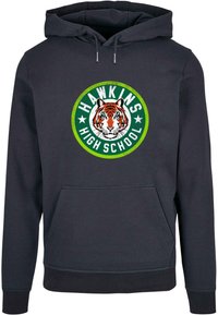 Tmavomodrá mikina s kapucňou a prednou klokankou. Obsahuje okrúhly grafický motív so tigrom a textom "HAWKINS HIGH SCHOOL" v zelenej a bielej farbe.