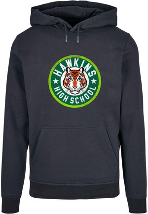 Tumši zils kapuce ar priekšējo kangaroo kabatu. Izceļas ar apaļu grafiku ar tīģeri un "HAWKINS HIGH SCHOOL" tekstu zaļā un baltā krāsā.