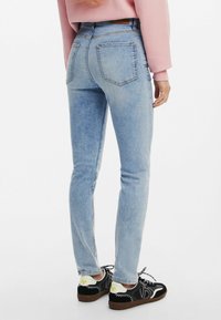Vaaleansiniset skinny-farkut, joissa on sileä denim-pinta, viisi taskua ja vetoketjukiinnitys, yhdistettynä mustiin lenkkareihin, joissa on valkoisia yksityiskohtia.