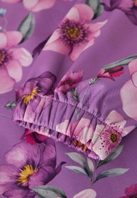 Lilla stoff med elastisk mansjett som har et rosa og lilla blomster mønster med grønne blader og gule blomster sentre.