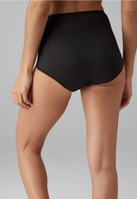 Culotte noire taille haute avec une texture lisse et une taille élastique, dotée de coutures plates pour réduire la visibilité sous les vêtements.