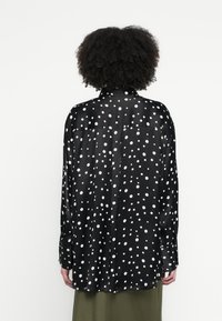 Fekete, hosszú ujjú, selymes anyagból készült ing, fehér pöttyös mintával, látható hátsó vállrésszel és ívelt szegéllyel.