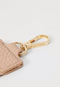 Chaveiro de couro em bege claro, apresentando um acabamento texturizado. Acessórios em metal dourado com um fecho, gravado com "VALENTINO."