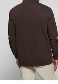 Brun, ribbad tyg sweatshirt med hög krage, långa ärmar och en avslappnad passform. Har en enkel design utan utsmyckningar.