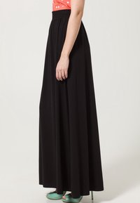 Jupe maxi noire avec une taille élastique, fabriquée en tissu doux. Complétée par des chaussures vert menthe. Design simple, longueur au sol.