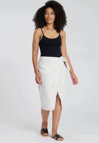 Zonder bandjes zwart top, witte wikkelrok met verticale zwarte strepen, rafelige zoom, vastgebonden in de taille. Zwarte sandalen maken de outfit compleet.