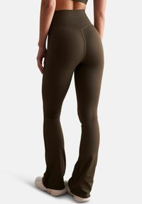 Leggings taille haute en olive ondulé avec un design à jambes évasées et une texture lisse, associés à des chaussures de sport blanches.