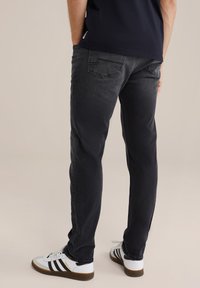 Crne traperice slim fit kroja, s stražnjim džepovima i suptilnim detaljima šavova, uparene s bijelim tenisicama s crnim prugama.