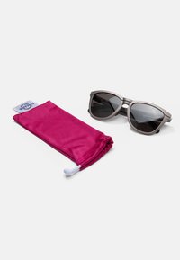 Ochelari de soare cu lentile gri și rame geometrice, acompaniați de un sac cu șnur fuchsia dintr-un material fin.