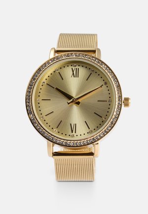 Montre dorée avec un cadran rond, finition satinée, chiffres romains aux positions 12 et 6, ornements en cristal et bracelet en maille.