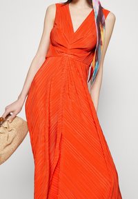 Faltendes Maxikleid in leuchtendem Orange mit V-Ausschnitt und Empire-Taille. Enthält ein farbenfrohes Schal-Accessoire. Die Textur ist glatt und fließend.