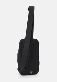 Borsa a tracolla nera di forma rettangolare, con una tracolla texturizzata e un compartimento con zip. Logo visibile nella parte anteriore.
