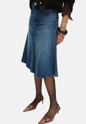 Denim A-line skirt in medium blue with a raw hem. Paired with brown heeled shoes and black patterned top. Smooth texture and casual fit.