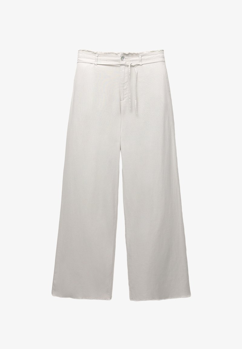 Pantalon blanc à jambes larges avec un bouton devant, des passants pour ceinture et un cordon fin à la taille sur un fond uni.
